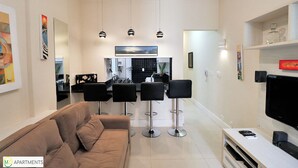 A modern living room with a sofa, a TV, and a kitchen in the background. - MZ Apartments Leme III (Rio de Janeiro)