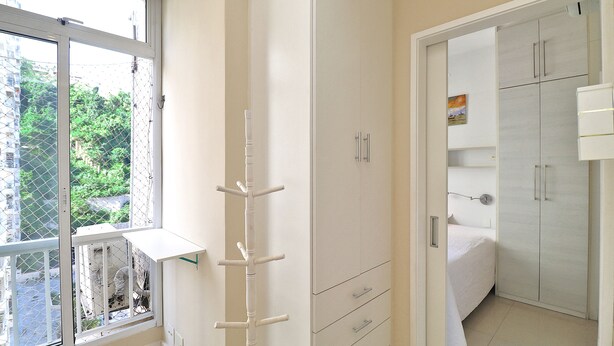 A bedroom with a large wardrobe, a bed, and a window with a view of greenery. - MZ Apartments Leme III (Rio de Janeiro)