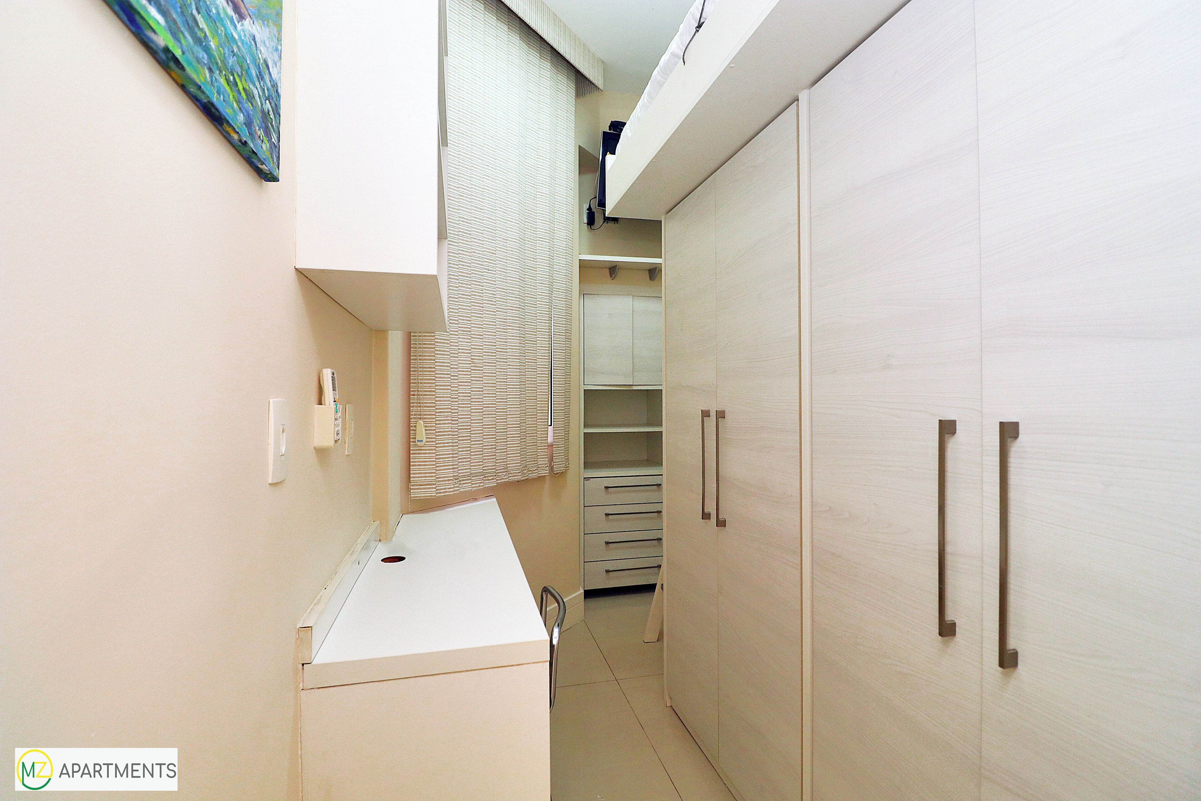 Un couloir étroit avec une kitchenette, un dressing et une fenêtre équipée de stores.