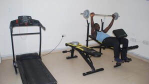 Un gimnasio con cinta de correr, banca para press de banca y una persona haciendo press de banca.