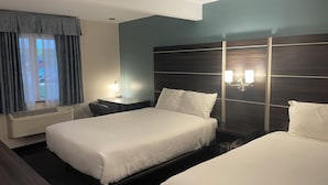 A hotel room with two beds, a desk, a chair, a lamp, and a window with curtains. - Landmark Inn (Osawatomie)
