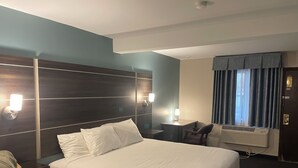 A hotel room with a large bed, a desk, a chair, and a window with curtains. - Landmark Inn (Osawatomie)