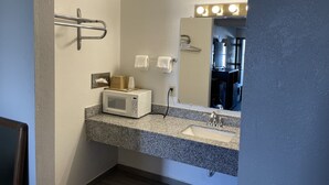 A bathroom with a granite countertop, a microwave, a sink with a vanity mirror, and a towel rack.