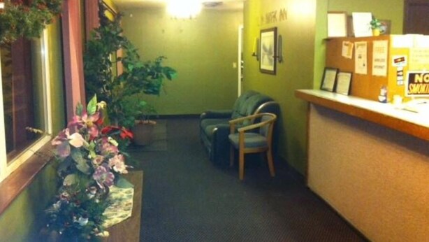 A reception area with a desk, chairs, a plant, and a wall with a 'No Smoking' sign. - Landmark Inn (Osawatomie)