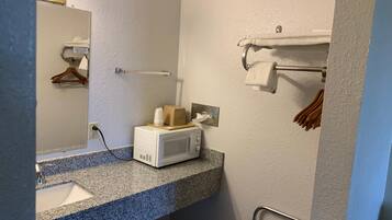 Un baño con encimera de granito, lavabo blanco, espejo, toallero y microondas.
