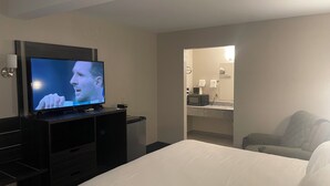 A hotel room with a bed, a television, a desk, and a bathroom visible through an open door.