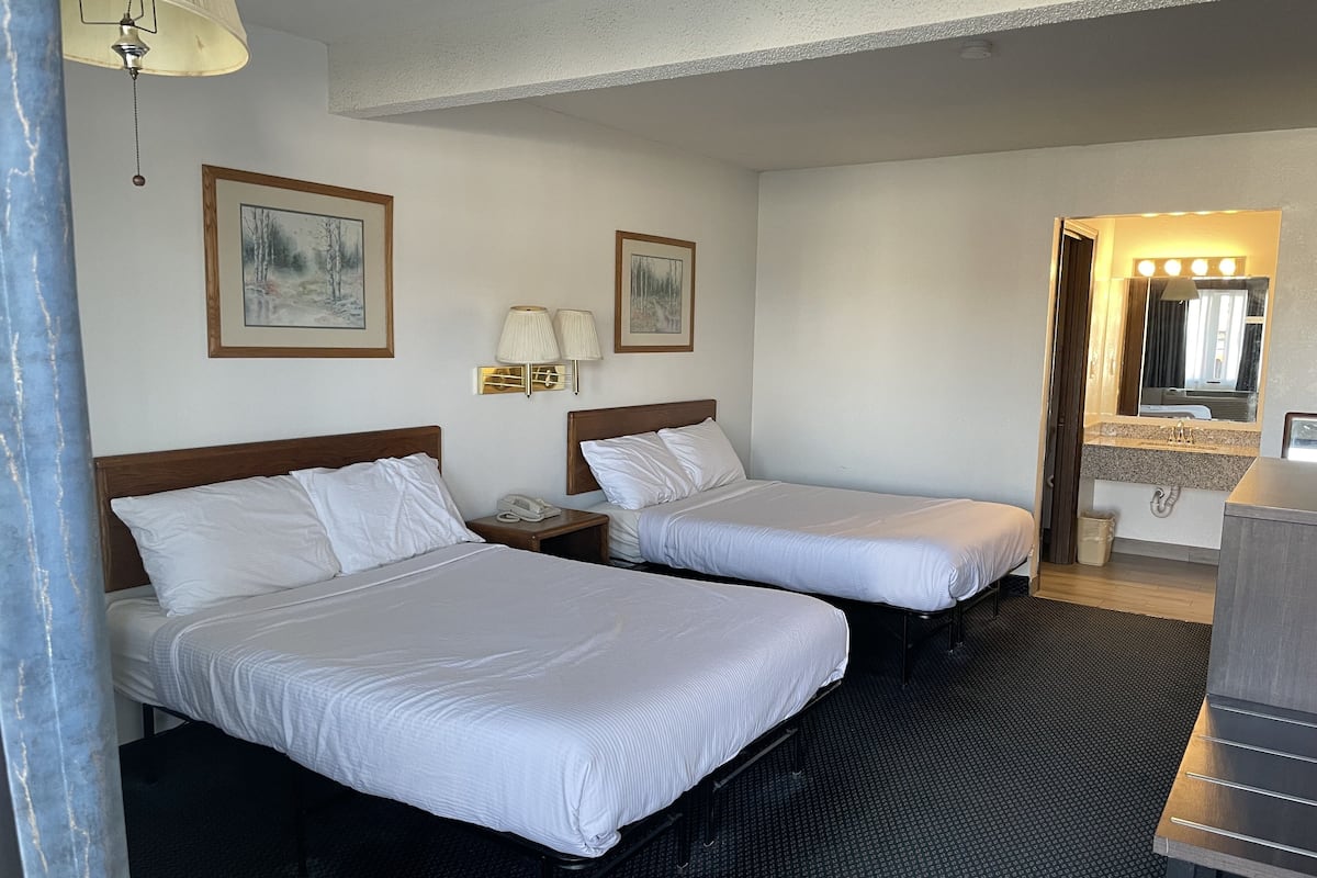 A hotel room with two beds, a bathroom with a sink and mirror, and wall-mounted lamps.