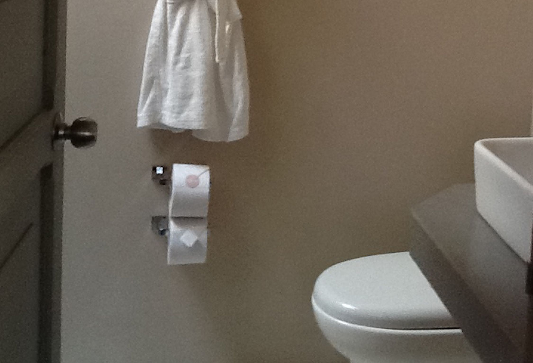 Un baño con inodoro, una toalla colgada en la pared y un dispensador de toallas de papel.