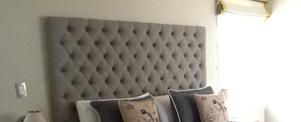 A bedroom with a tufted headboard, a bedside table, and two pillows.