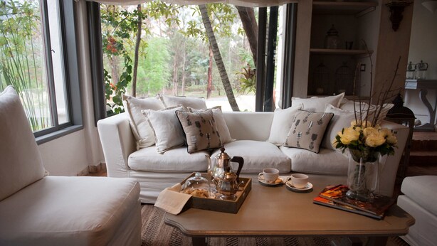 Una sala de estar acogedora con un sofá, una mesita de centro con una bandeja, un jarrón con flores y vistas al verdor exterior.