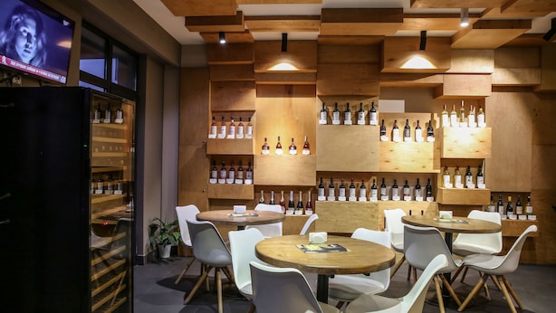 A modern bar area with wooden shelves displaying bottles, white chairs around tables, and a television on the left. - Wine Hotel (Chisinau)
