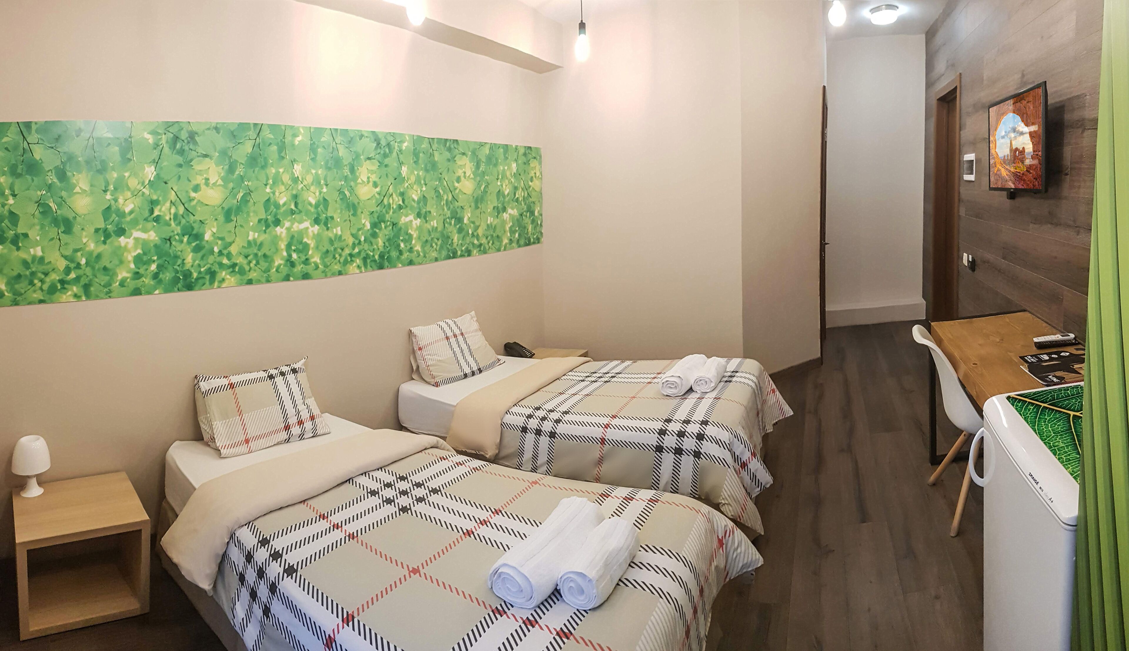Hotelkamer met twee bedden, een klein tafeltje, een stoel, een televisie aan de muur en een abstract schilderij in groentinten.