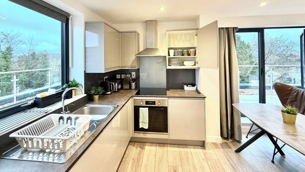 A modern kitchen with a built-in oven, a sink, and a dining area with a table and chairs. - Hampton Suites Serviced Apartments (Thames Ditton)
