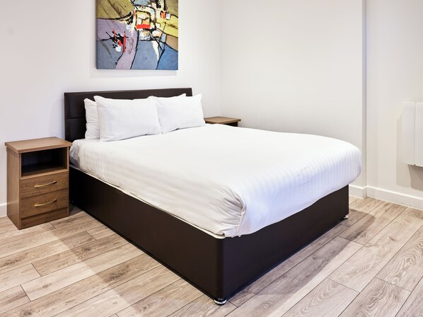 Un dormitorio moderno con una cama grande, una mesita de noche de madera, una pequeña mesita auxiliar y un cuadro abstracto colorido en la pared.