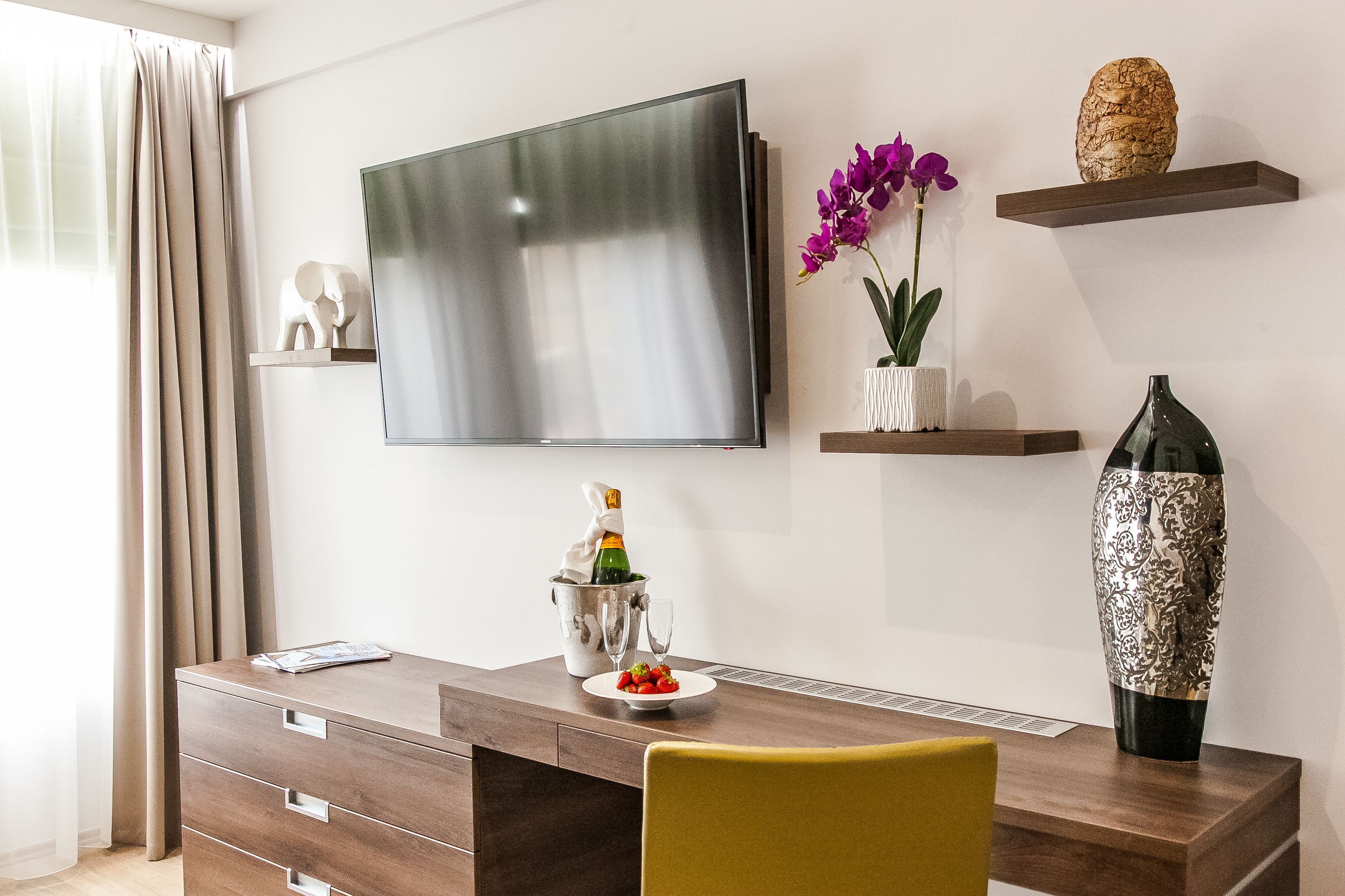 Una sala moderna con un televisor de pantalla plana, una mesa de centro de madera, un sillón amarillo y objetos decorativos como un jarrón y una escultura.