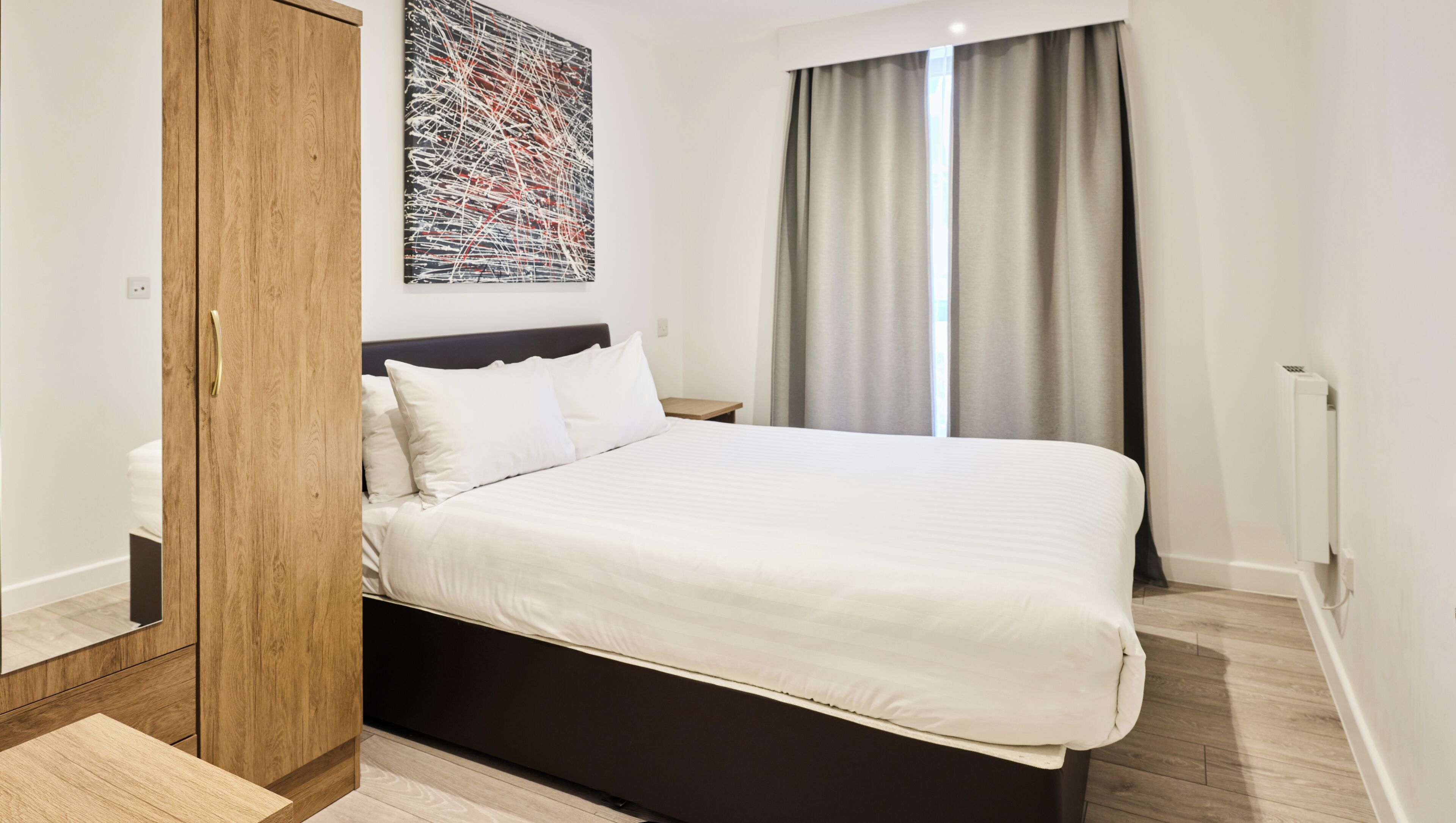 Ett modernt hotellrum med en stor säng, ett träskåp och en stor, abstrakt målning på väggen.