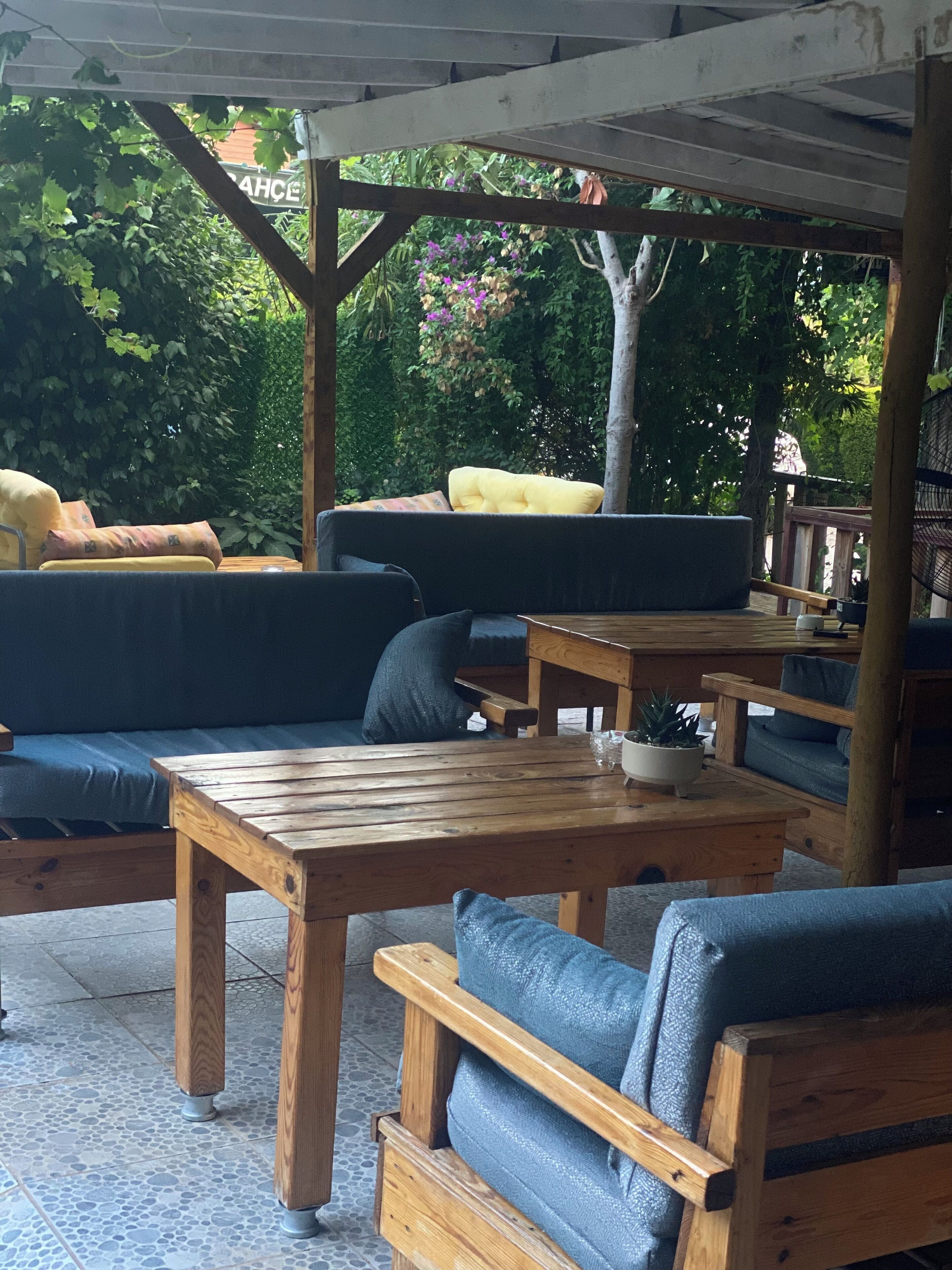 An outdoor seating area with wooden tables and blue cushioned sofas under a wooden pergola.