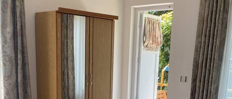 A bedroom with a bed, a wooden wardrobe, a bench, and a view of the outside.