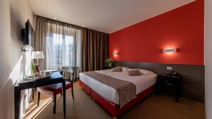Una habitación de hotel con una cama, un escritorio, una silla, un televisor y una mesita de noche.