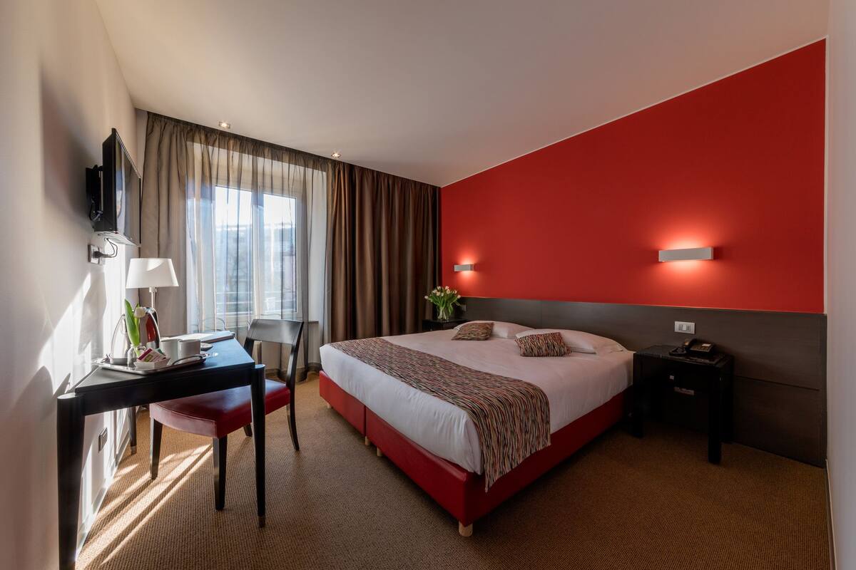 Una habitación de hotel con una cama, un escritorio, una silla, un televisor y una mesita de noche.