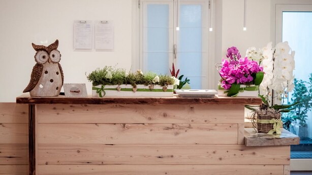 Un mostrador de recepción con detalles de madera, un búho decorativo y un arreglo floral.