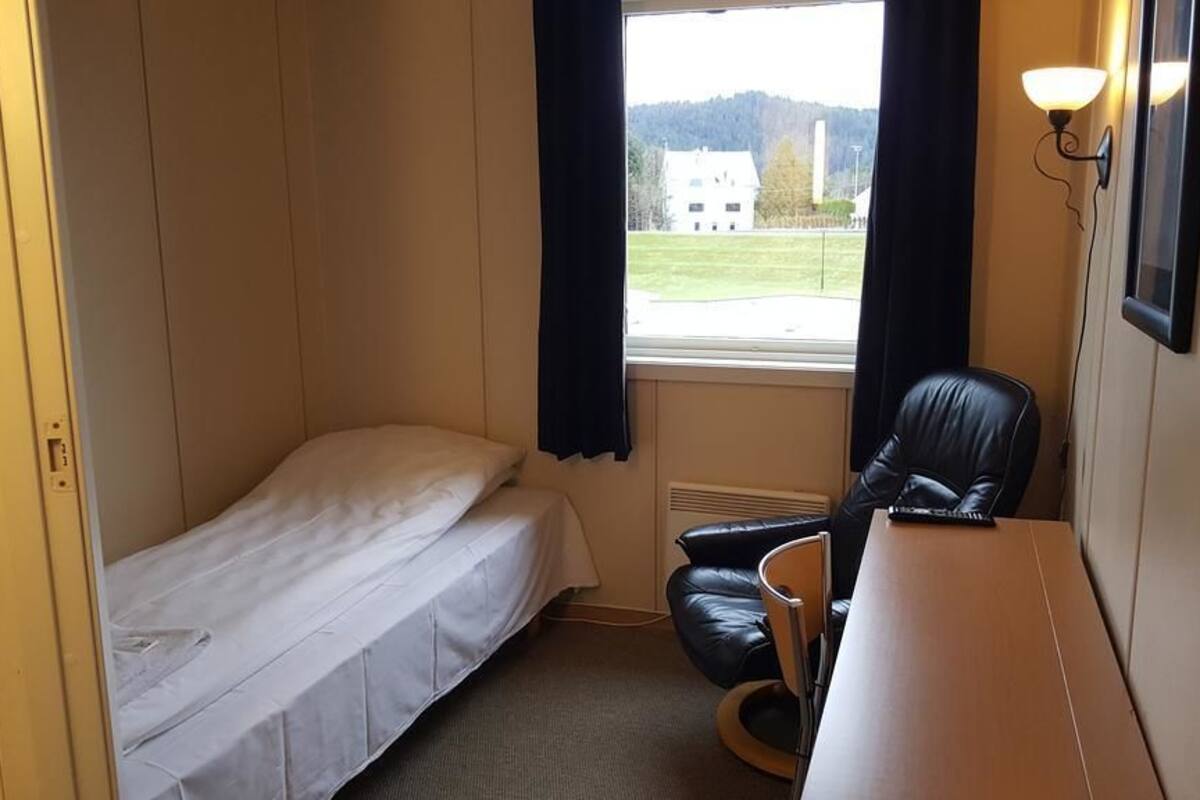 Una habitación pequeña con una cama individual, una silla, un escritorio y una ventana con cortinas.