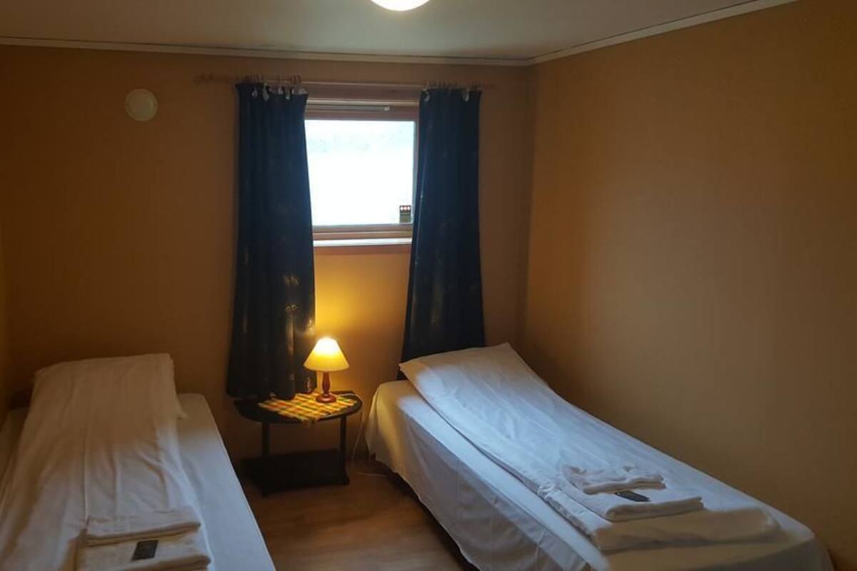 Habitación pequeña de hotel, con capacidad para una persona, equipada con dos camas individuales, una mesita de noche con lámpara y una ventana con cortinas.