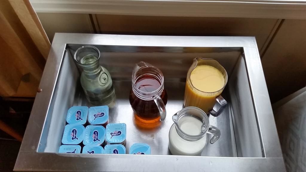 Una bandeja de acero inoxidable con recipientes de yogur, una jarra de miel, un jarro de leche y un vaso de zumo de naranja.