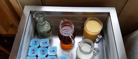 Una bandeja de acero inoxidable con recipientes de yogur, una jarra de miel, un jarro de leche y un vaso de zumo de naranja.
