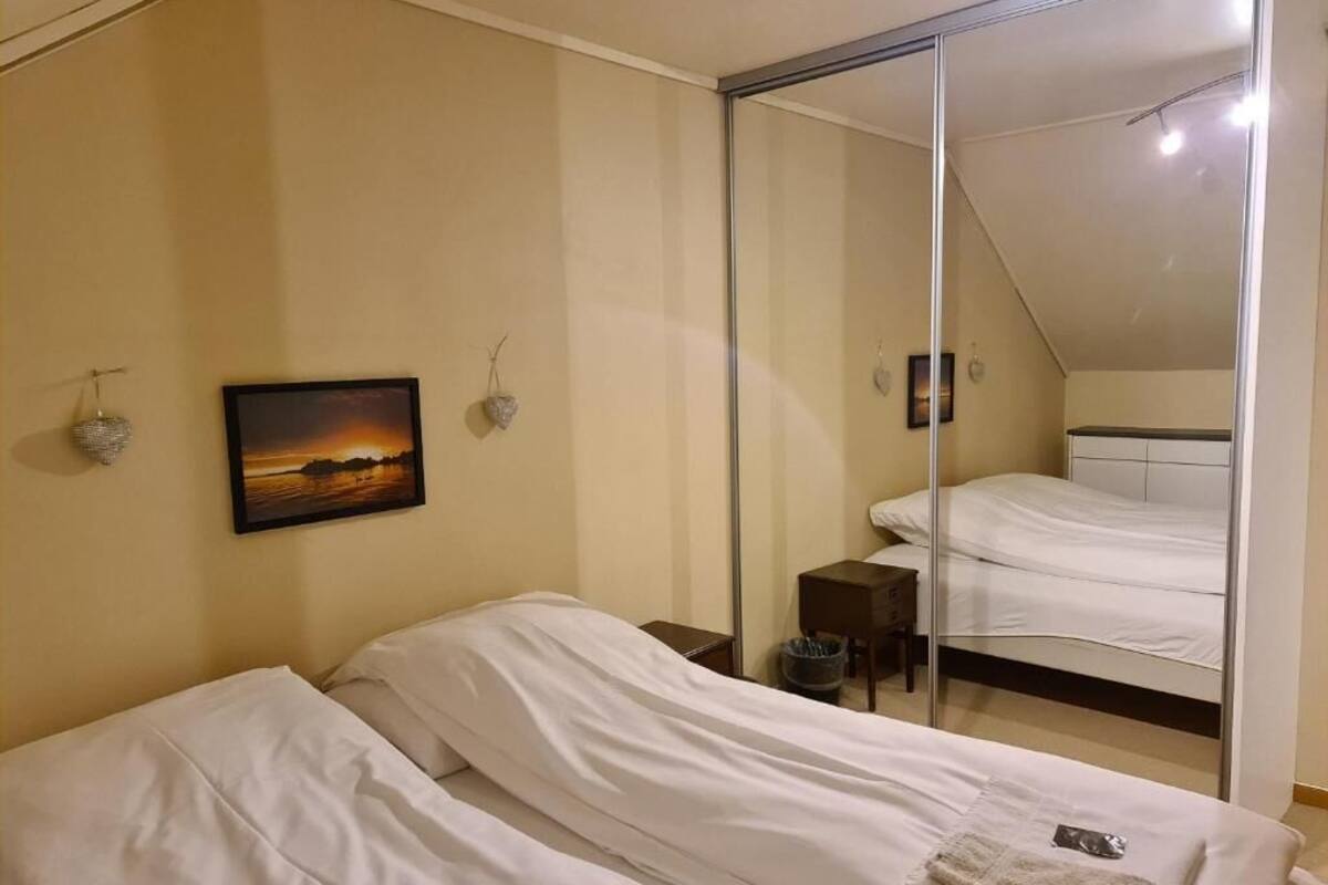 Un dormitorio con dos camas individuales, una mesita de noche, un pequeño tocador, un cuadro enmarcado en la pared y un ventanal corredero que da a otra habitación.