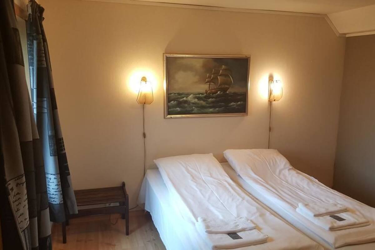 Una habitación con dos camas, un cuadro en la pared y dos lámparas adosadas.