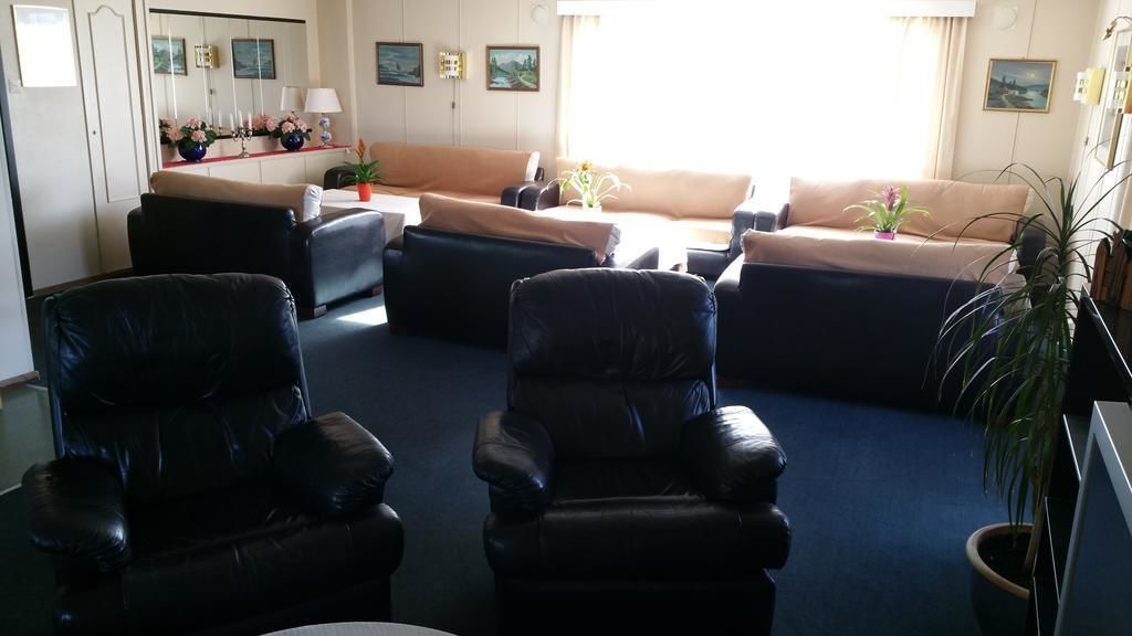 A living room with a sofa, two armchairs, a coffee table, and a TV. There are potted plants and framed pictures on the walls.