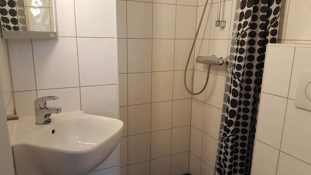 A bathroom with a white sink, a shower with a black and white polka dot shower curtain, and white tiled walls.