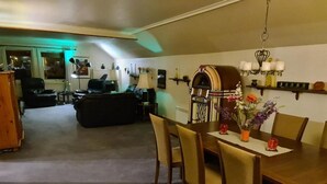 Un comedor con mesa y sillas de madera, un jukebox y una araña.