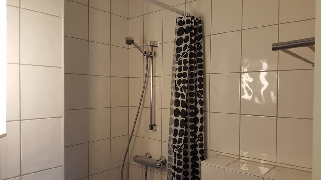 Um chuveiro com cortina de chuveiro estampada em bolinhas, um chuveiro manual e uma torneira fixa na parede.
