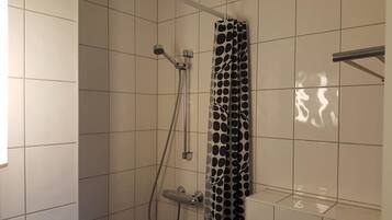 Um chuveiro com cortina de chuveiro estampada em bolinhas, um chuveiro manual e uma torneira fixa na parede.
