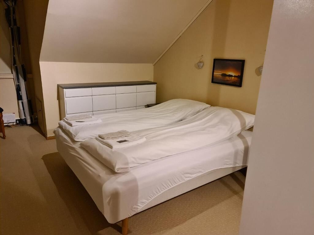 Un dormitorio con cama, cabecera, un cuadro en la pared y una escalera apoyada en la pared.