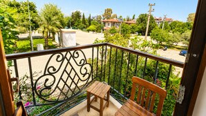 Un balcon avec une chaise et une table en bois, une rambarde en métal et une vue sur un quartier résidentiel avec des maisons et de la verdure.