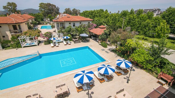 Une piscine entourée de bâtiments et de verdure, avec des chaises longues et des parasols.