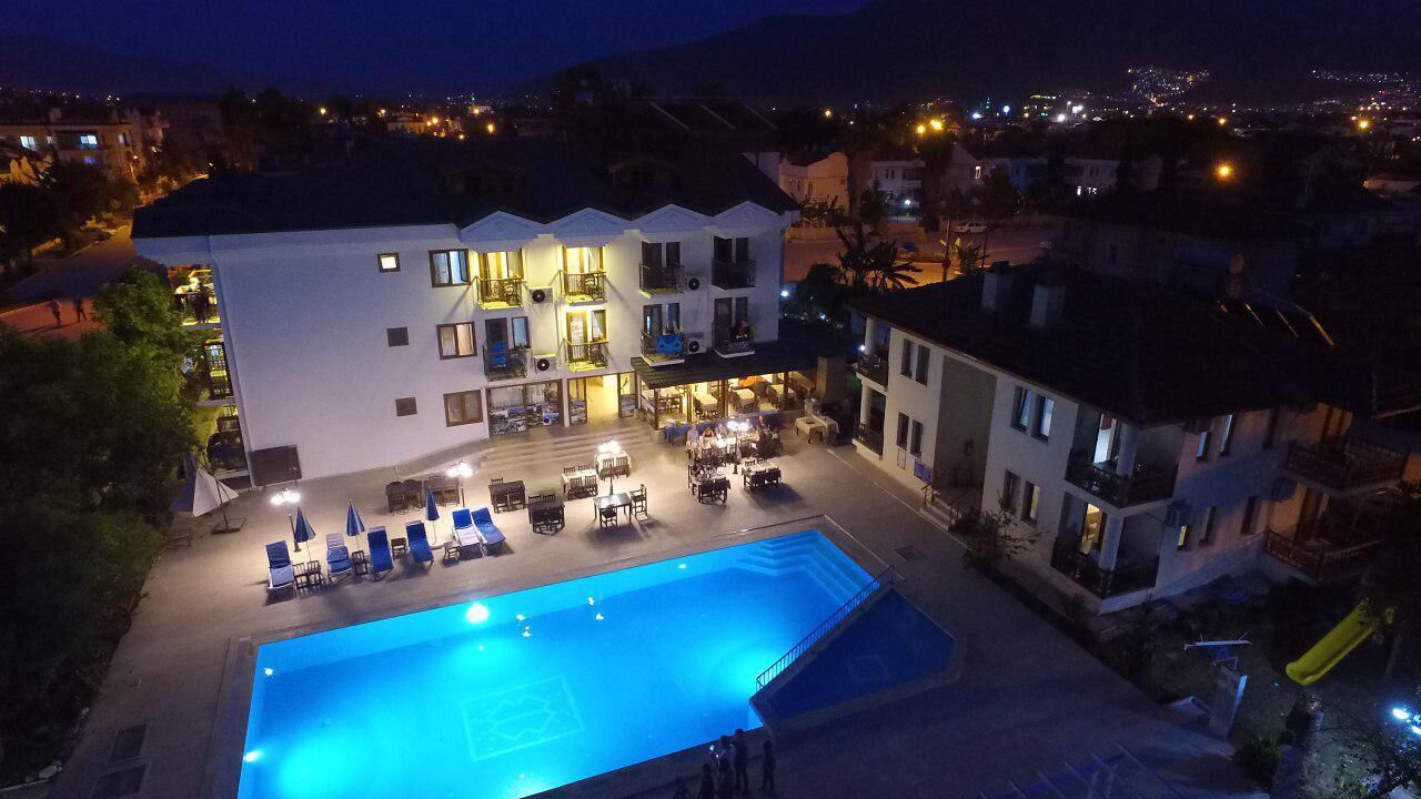 A hotel with a swimming pool, outdoor seating, and a view of the city at night.