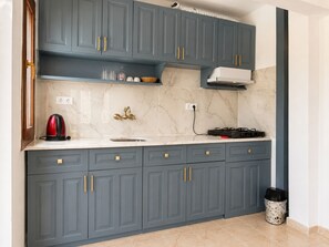 A kitchen with grey cabinets, a marble countertop, a gas stove, and a red kettle. - Kilim Apart Hotel (Fethiye)