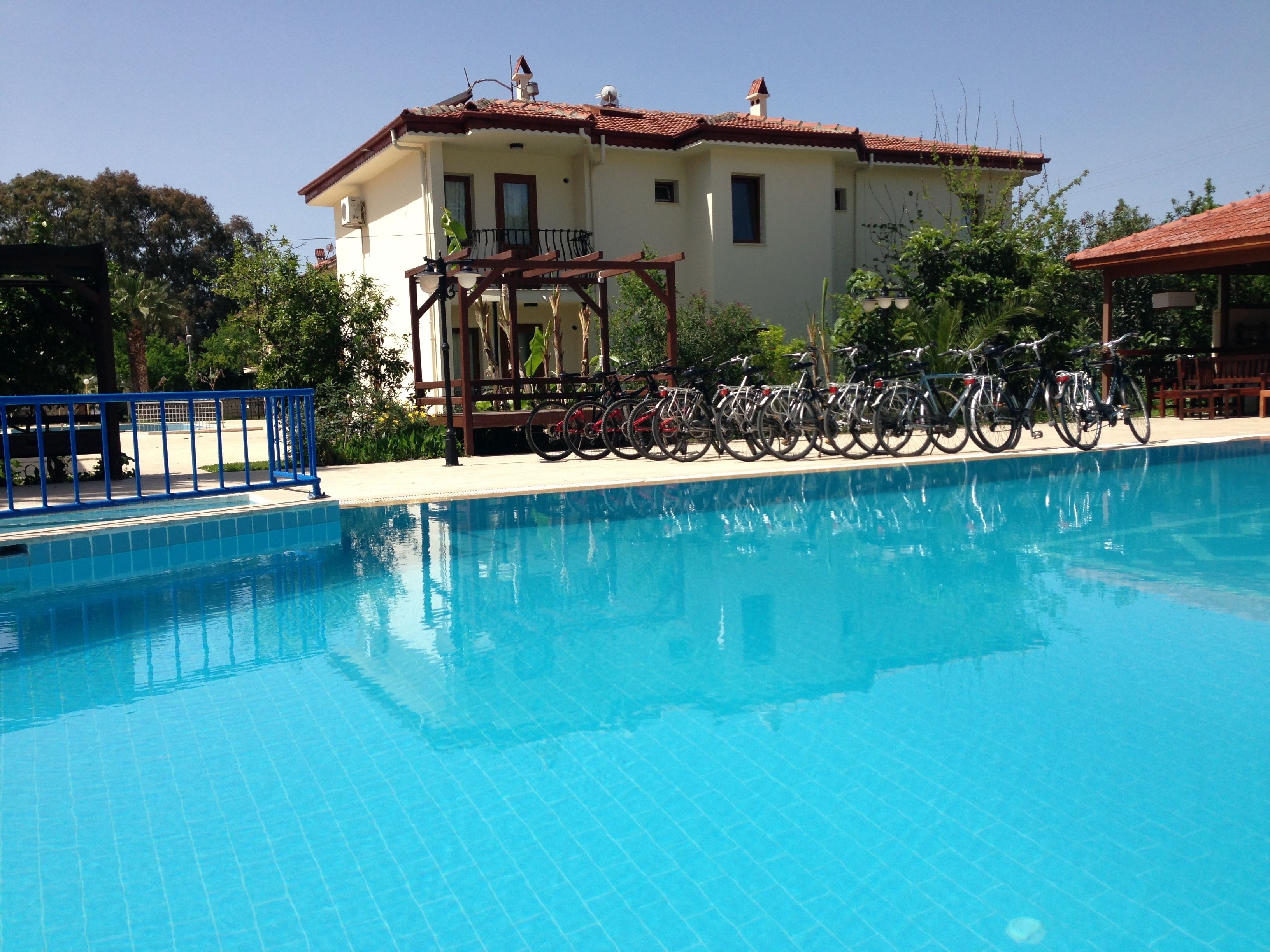 A swimming pool with bicycles parked nearby, a building with a tiled roof, and a clear sky.