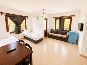 A room with a bed, a sofa, a small table with a remote control, a television, and a refrigerator. - Kilim Apart Hotel (Fethiye)