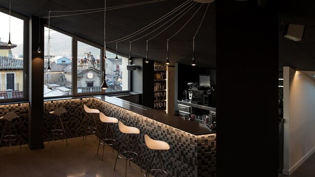 Un espace bar moderne avec un mur recouvert de carreaux foncés, des tabourets de bar et des luminaires suspendus.