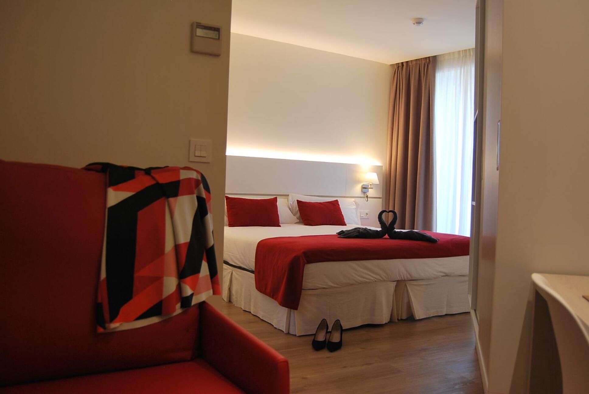 Een hotelkamer met een rode bank, een bed met rode beddengoed, en een paar schoenen op de vloer.