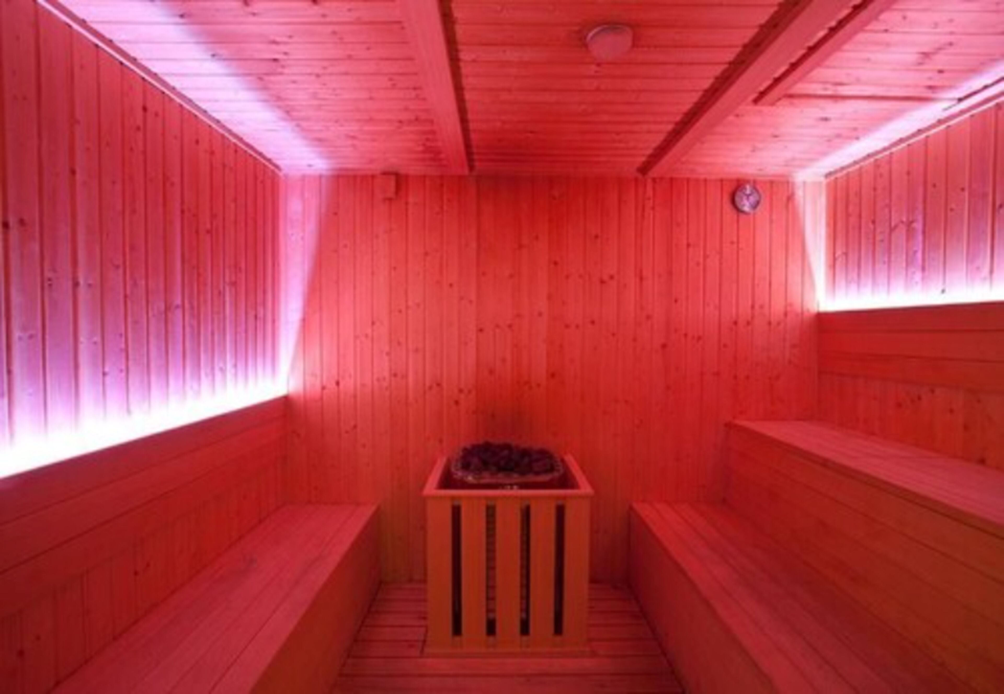 Una sauna con paredes y bancos de madera, un calentador central y un reloj en la pared.