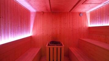 Una sauna con paredes y bancos de madera, un calentador central y un reloj en la pared.