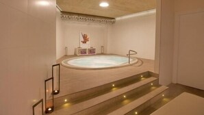 Un espace bien-être comprenant un jacuzzi, des marches menant à celui-ci et des appliques murales.