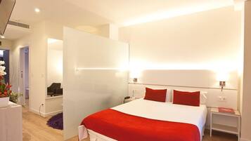 Una habitación de hotel moderna con una cama grande, paredes blancas y un detalle en rojo.