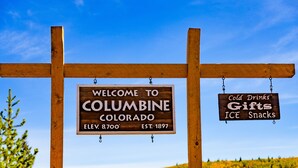 Un senyal de fusta amb dos cartells: "WELCOME TO COLUMBINE COLORADO" i "Cold Drinks Gifts ICE Snacks".